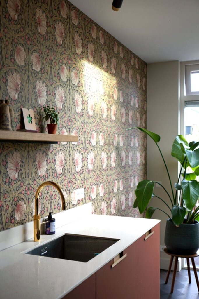 Rode keuken met wit marmer look keukenblad, decoratief bloemenprint behang. Goudkleurige kraan.