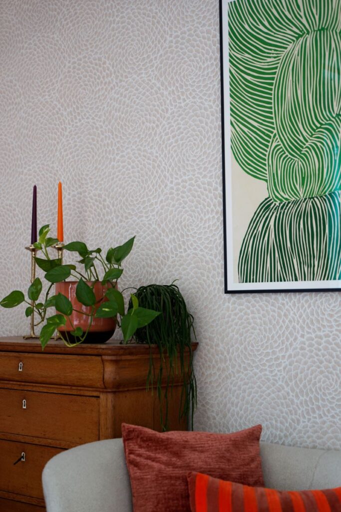 Decoratief print behang met groene abstracte kunst. Vintage kastje met accessoires en planten.