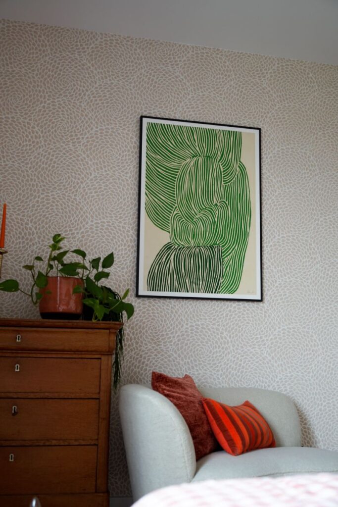 Decoratief print behang met groene abstracte kunst. Vintage kastje met accessoires en planten. Grijze fauteuil met decoratieve kussens.