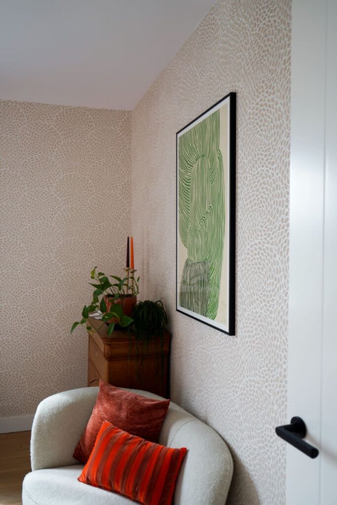 Decoratief print behang met groene abstracte kunst. Vintage kastje met accessoires en planten. Grijze fauteuil met decoratieve kussens.