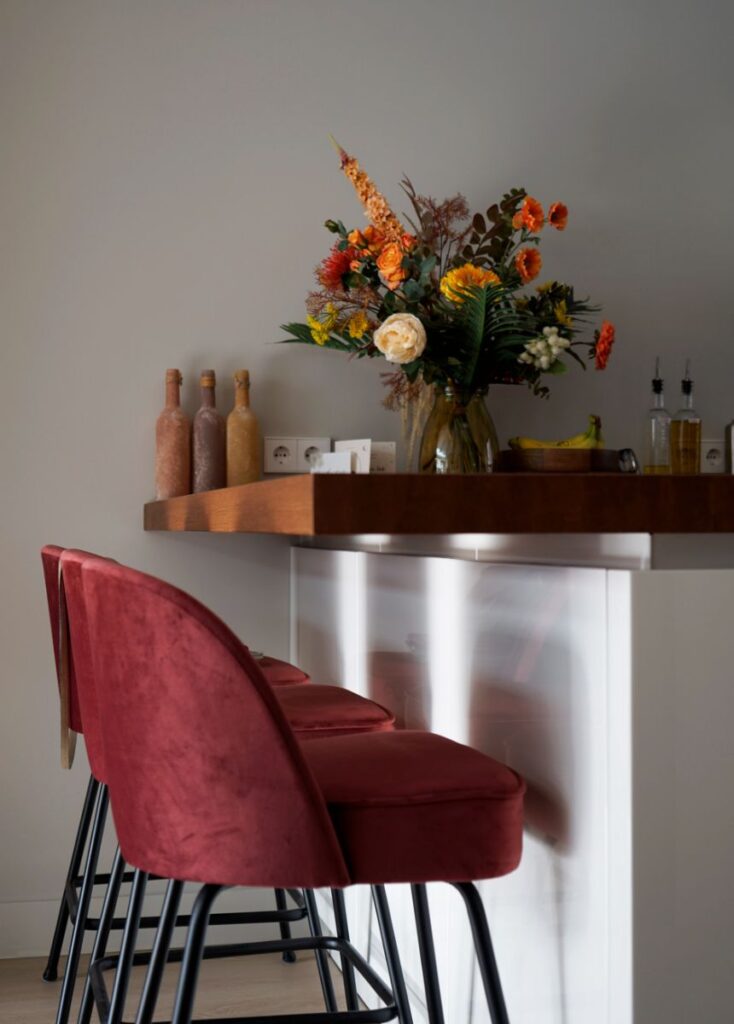 Rode barstoelen met een zwart onderstel en een houten blad als bar met accessoires hierop.