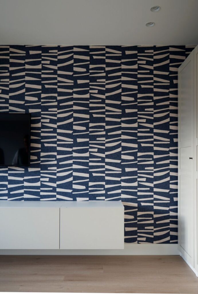 Donkerblauw met wit decoratief behang. Witte muren en lichte pvc vloer. Wit tv-meubel.