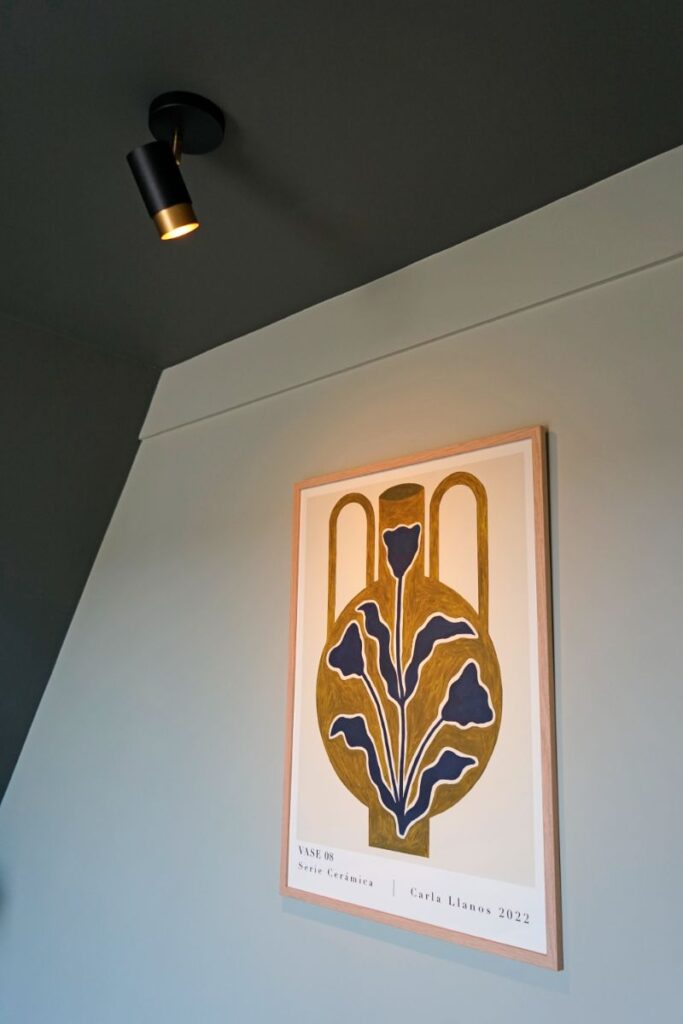 Slaapkamer met groene muren. Decoratief schilderij dat wordt uitgelicht door een plafondlamp.