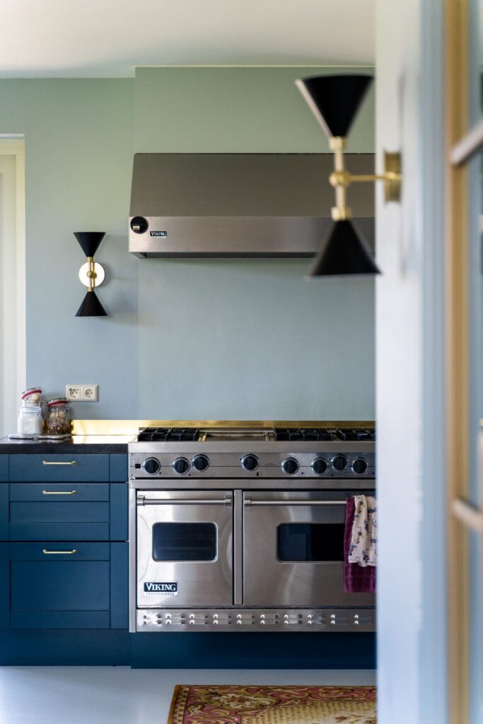 Donkerblauwe keuken met vintage fornuis en oven. Lichte vloer, muren en plafond. Up-down verlichting aan de wand.