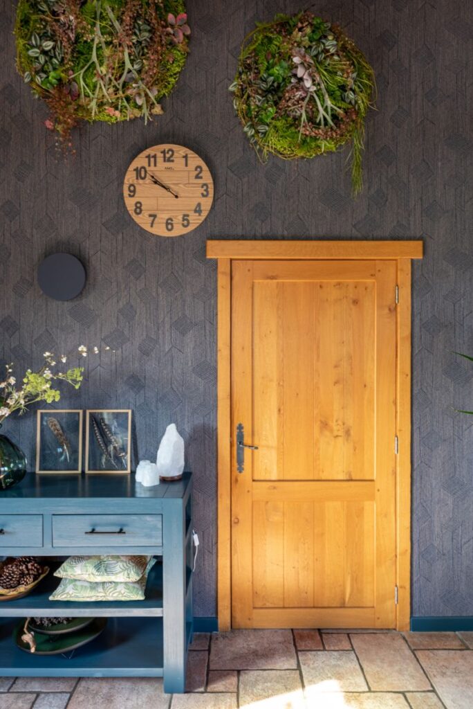 Wand met donkerblauw decoratief behang. Houten deur. Blauw geverfd houten kastje met accessoires. Natuur kunst aan de muur.