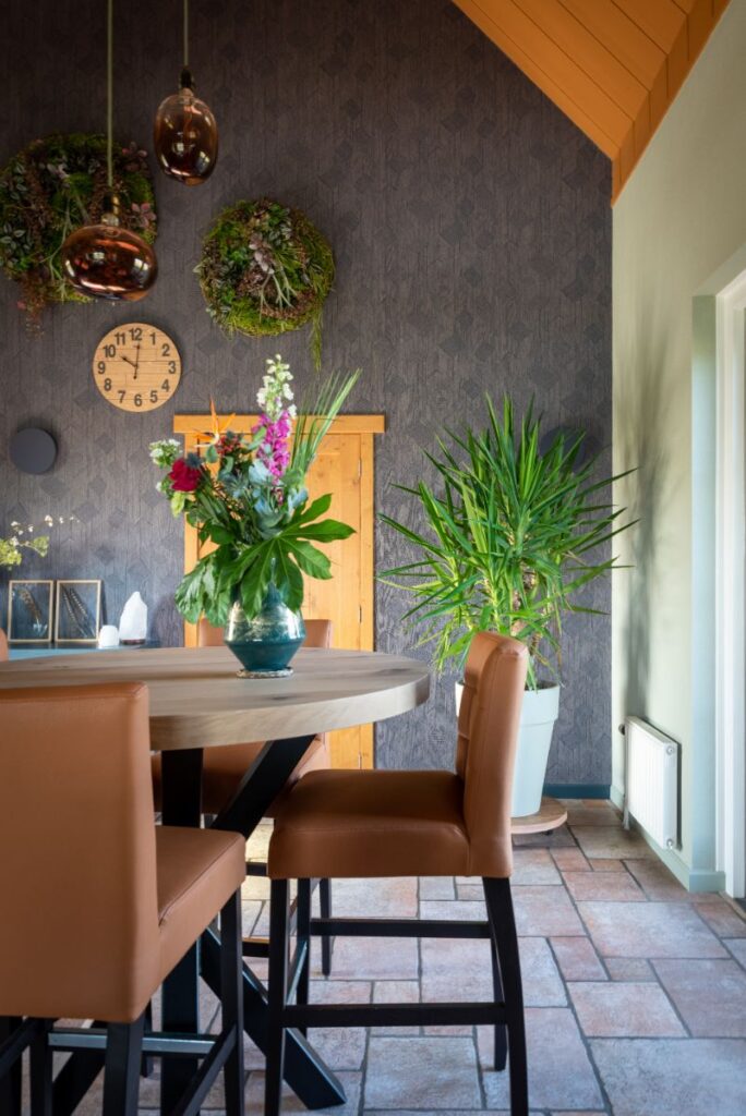 Stenen vloer met groene wand en decoratief donkerblauw behang. Ronde bar met barstoelen. Veel planten.