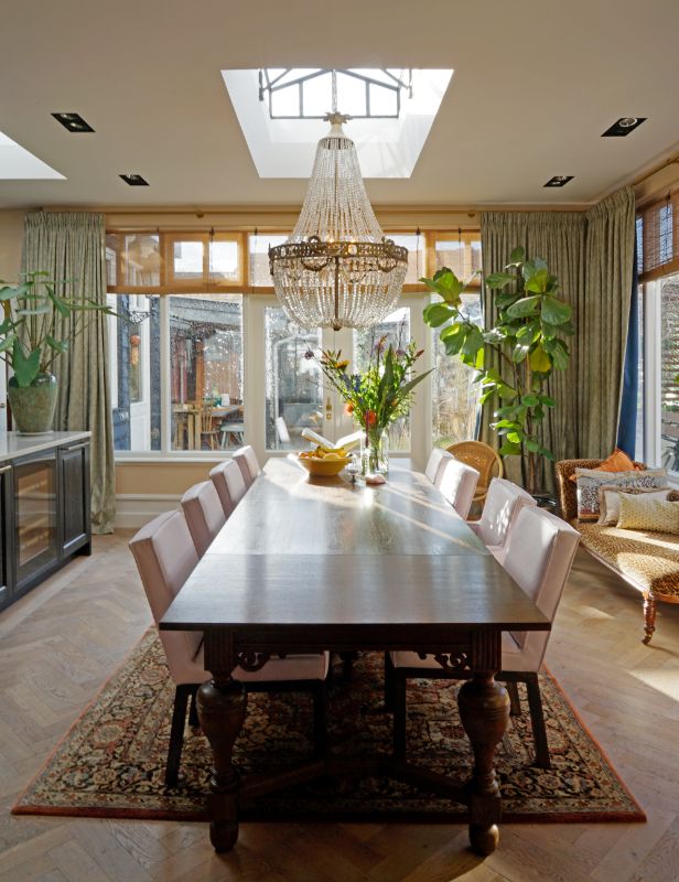 Eetkamer met grote vintage tafel en acht stoelen. Daklicht en een grote kroonluchter.