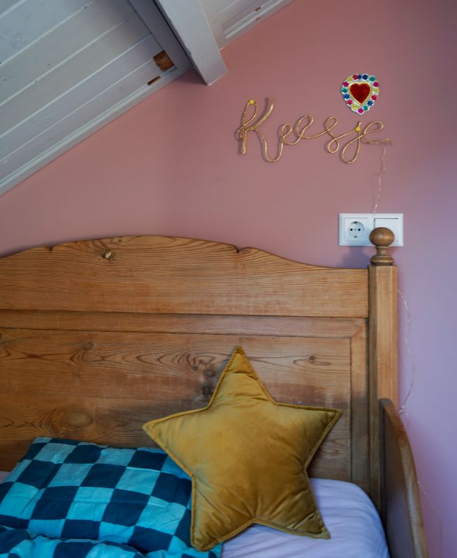 Vintage bed met gekleurd dekbedovertrek. Roze muur.