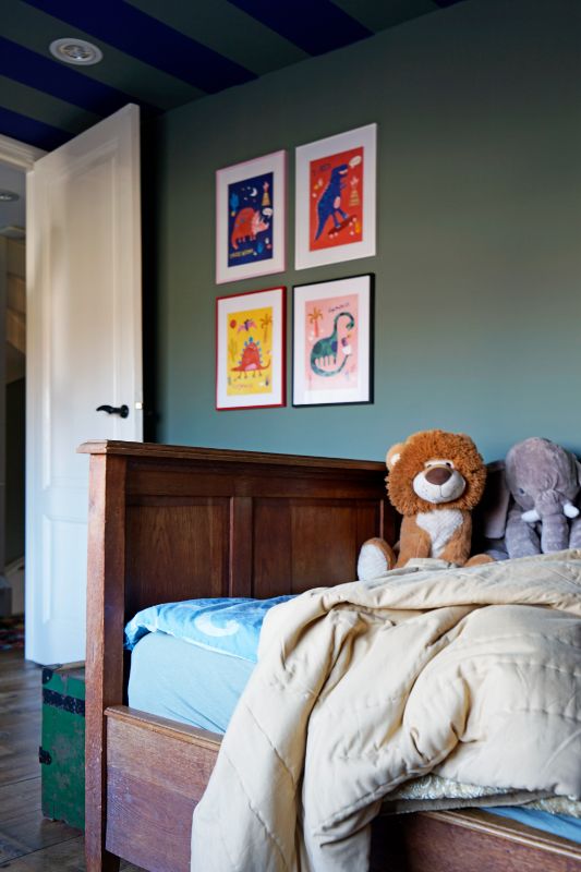 Jongenskamer met groene muur met schilderijtjes en een vintage bed met dierenknuffels.