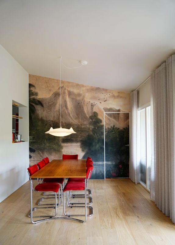 Eetkamer met decoratief behang en knal rode stoelen.