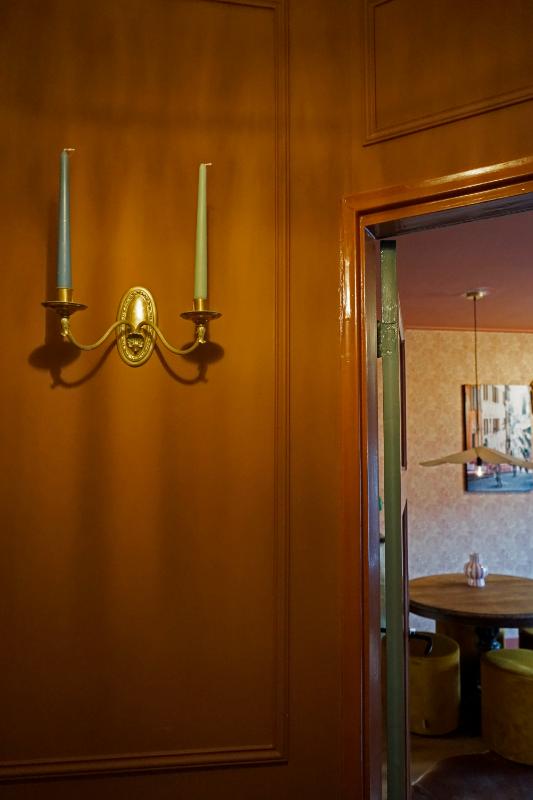 Roze wand met sierlijsten en een klassieke kandelaar. Doorkijk naar de kleurrijke kamer.