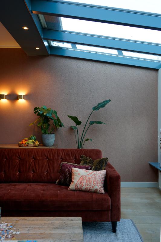 Blauw geschilderde kozijnen. Rode bank met lovi kussens. Wandlampen op de muur.