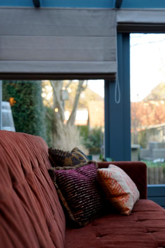 Blauw geschilderde kozijnen. Rode bank met LOVI kussens.