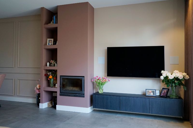 Roze wand met haard en open vakken. Tv meubel is zwevend.