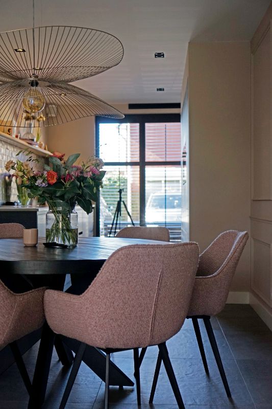 Zwarte houten eettafel et roze kuipstoelen.