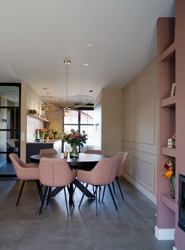 Roze wand met open vakken. Ronde eettafel met 6 roze kuipstoelen.