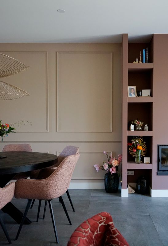 Lichte muur met lijsten. Roze wand met open vakken. Roze kuipstoelen.