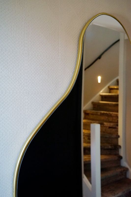 Doorkijk naar de trap door gouden organische spiegel.