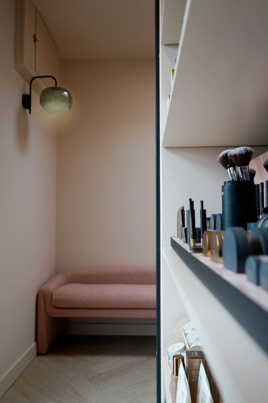 Roze bank, groene wandlamp en beauty producten.