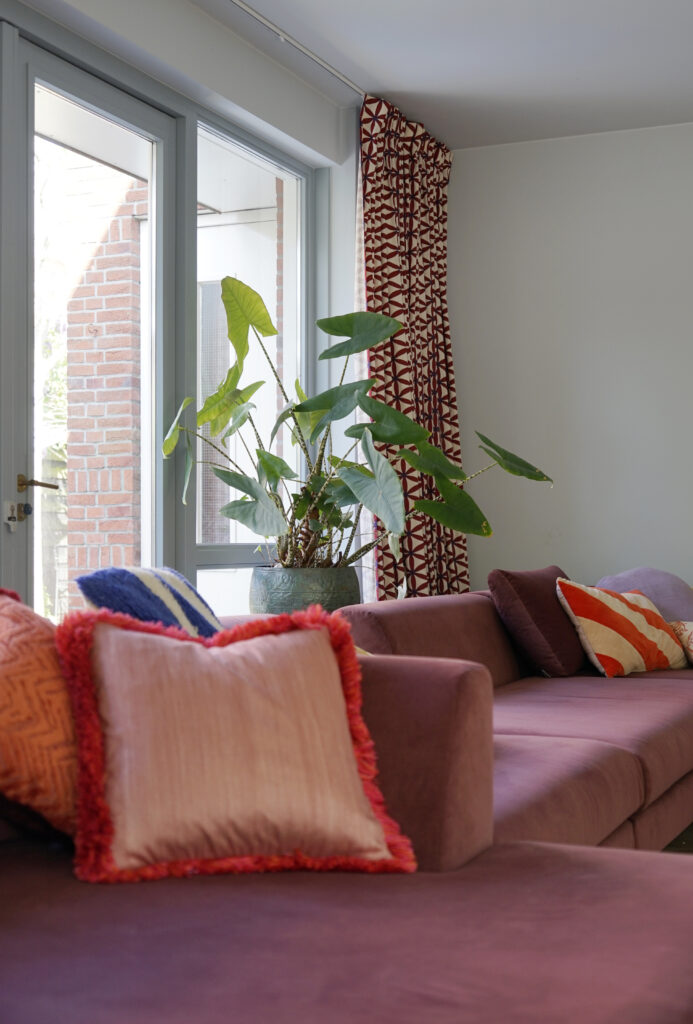 Roze modulaire bank met gekleurde kussens. Gordijn in een rood met witte patroonstof.