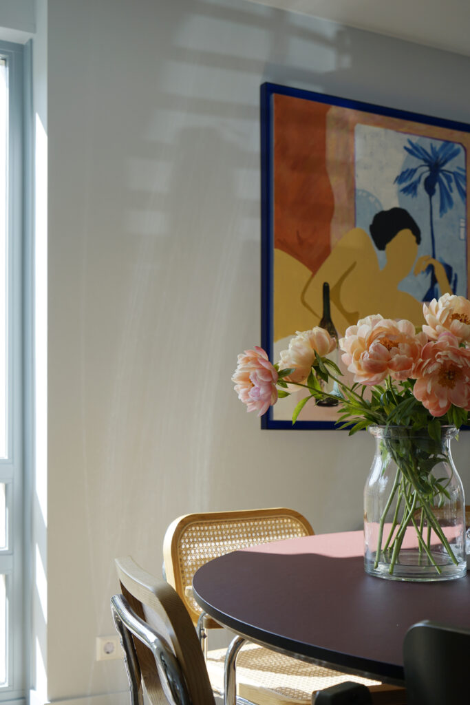 Bordeaux rode eettafel met rotan stoelen. Aan de wanden een kleurrijk schilderij.