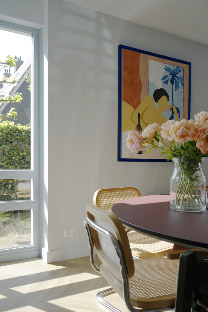 Lichtblauwe wanden. Bordeaux rode eettafel met rotan stoel.