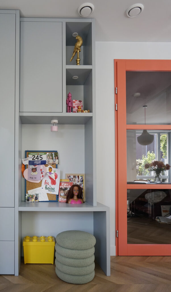 Lichtblauwe vakkenkast met kinderspeelhoek. Oranje glazendeur in de woonkamer.