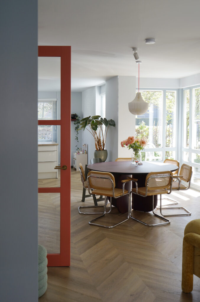 Licht blauwe muren. Ronde eettafel met rotan stoelen.