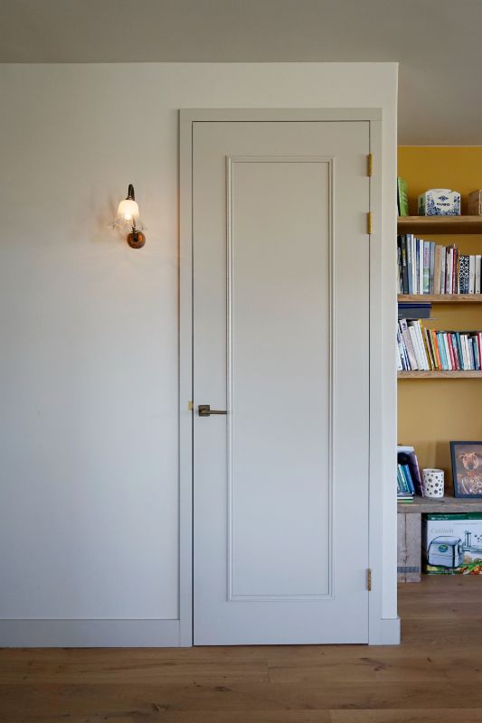 Deur met sierlijsten, ruw brons deurbeslag en een vintage wandlamp.