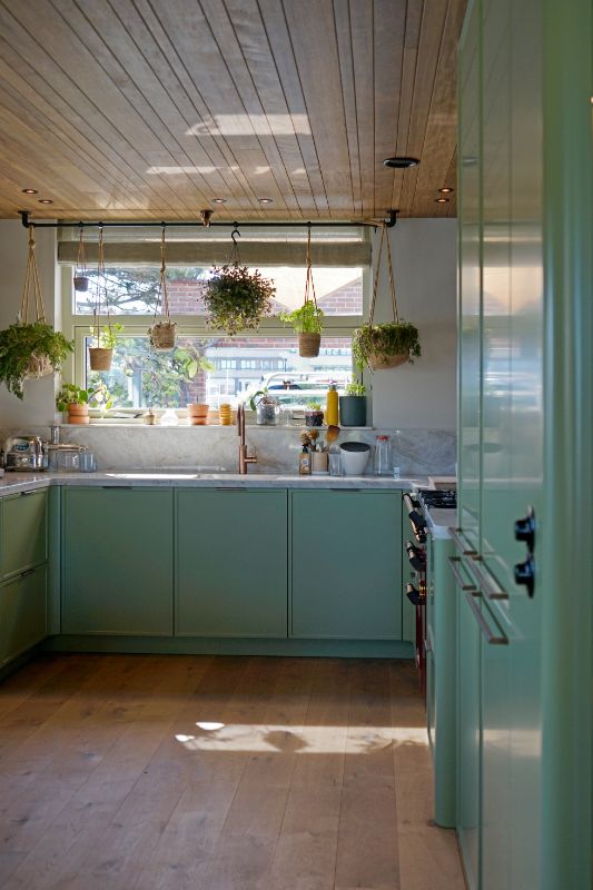 Groene maatwerk keuken. Houten plafond met verschillende hangplanten.