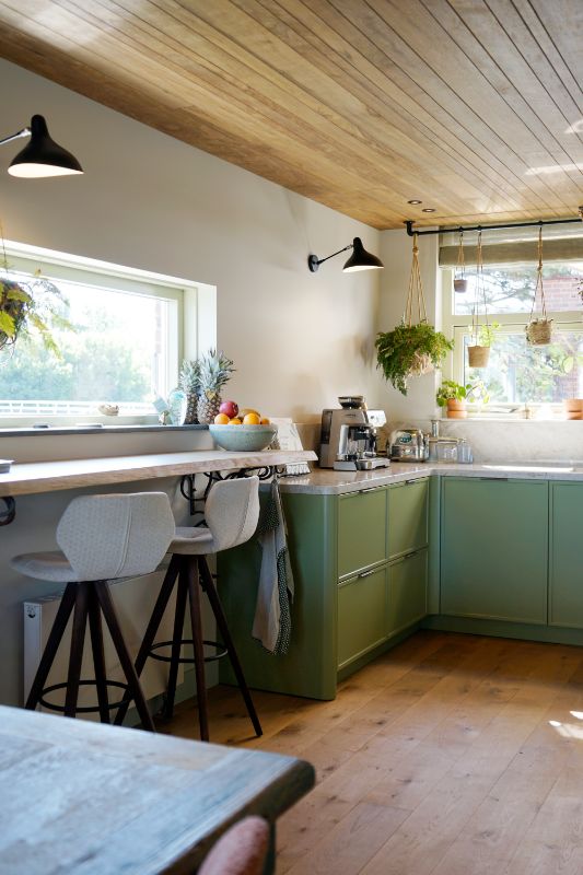 Groene maatwerk keuken met hieraan vast een bar met twee barstoelen.