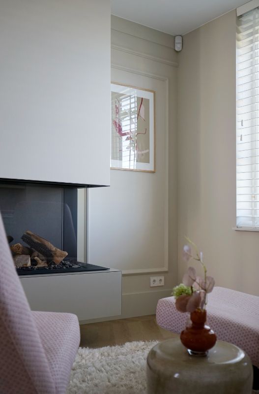 Strakke haard, beige wanden en roze fauteuils.
