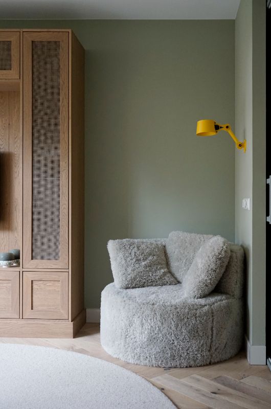 Fluffy fauteuil met gele leeslamp en houten maatwerk tv kast.