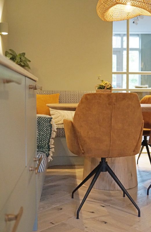 Ronde eettafel met eetkamerbank in patroonstof en gele stoelen.
