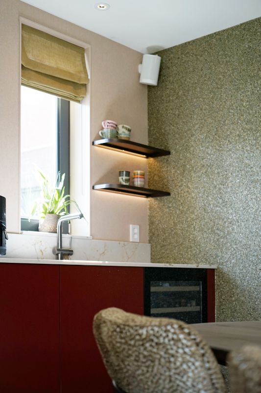 Rode keuken met licht marmer werkblad. Aan de wand twee wandplanken met koffie kopjes erop.
