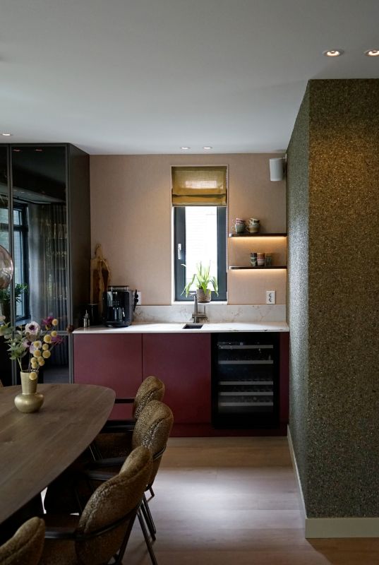 Rode keuken met wijnklimaatkast. Geelgroene vouwgordijnen in de dag van het kozijn.